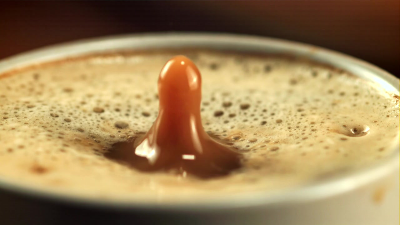 Goccia di caffè al rallentatore che schizza in un latte schiumoso