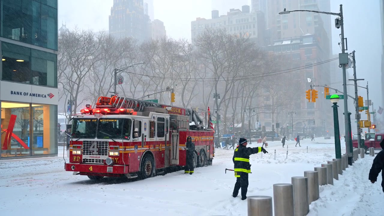 New York, ABD, 25 Aralık 2025: New York'ta karlı bir caddede park etmiş kırmızı itfaiye aracı. Yoğun kış fırtınası sırasında karla kaplı yolda gökdelenlerin yakınında duran acil durum aracı.