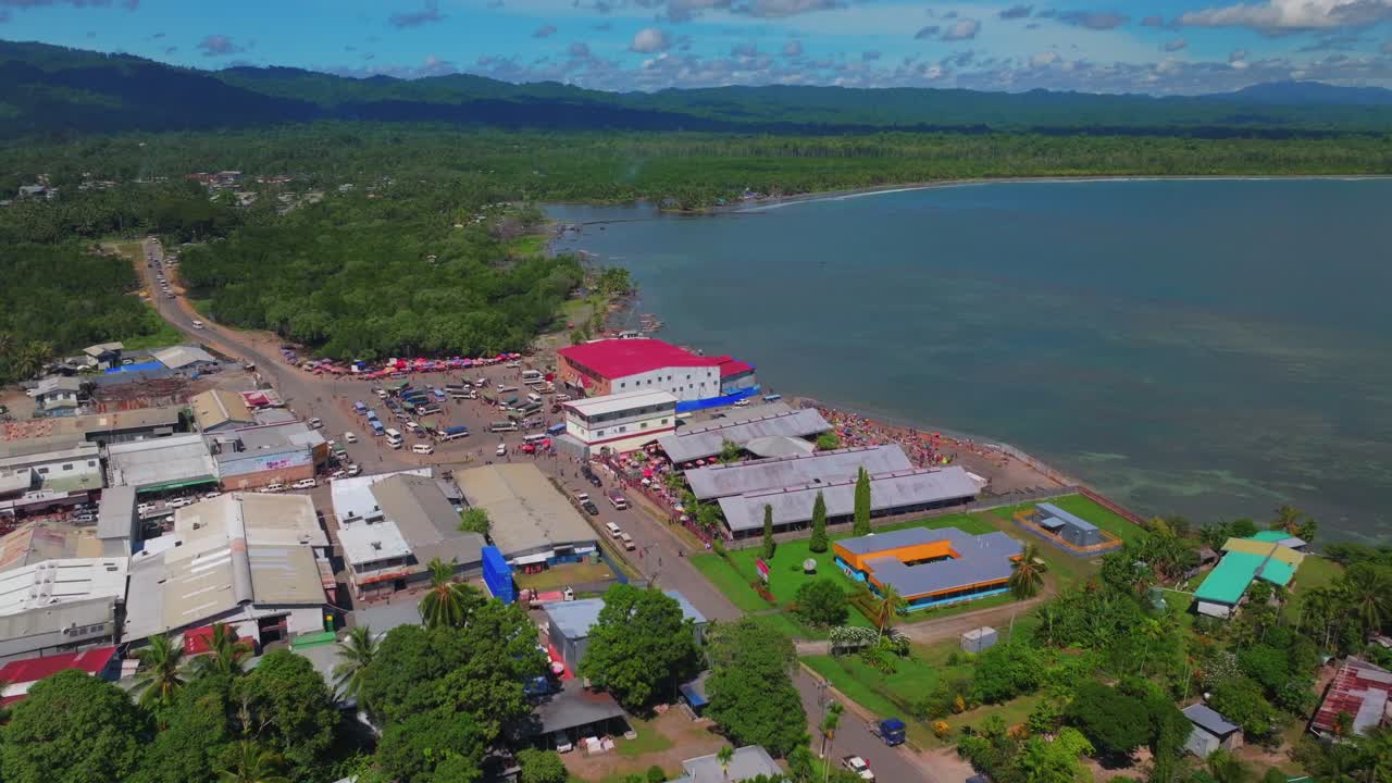 Fish Market Wewak Hill cars buildings people Boram road Wewak Papua New Guinea aerial drone downtown coastal town Sundaun Market Dogreto Bay Cape Wom Bismark Sea sunny blue sky morning forward motion