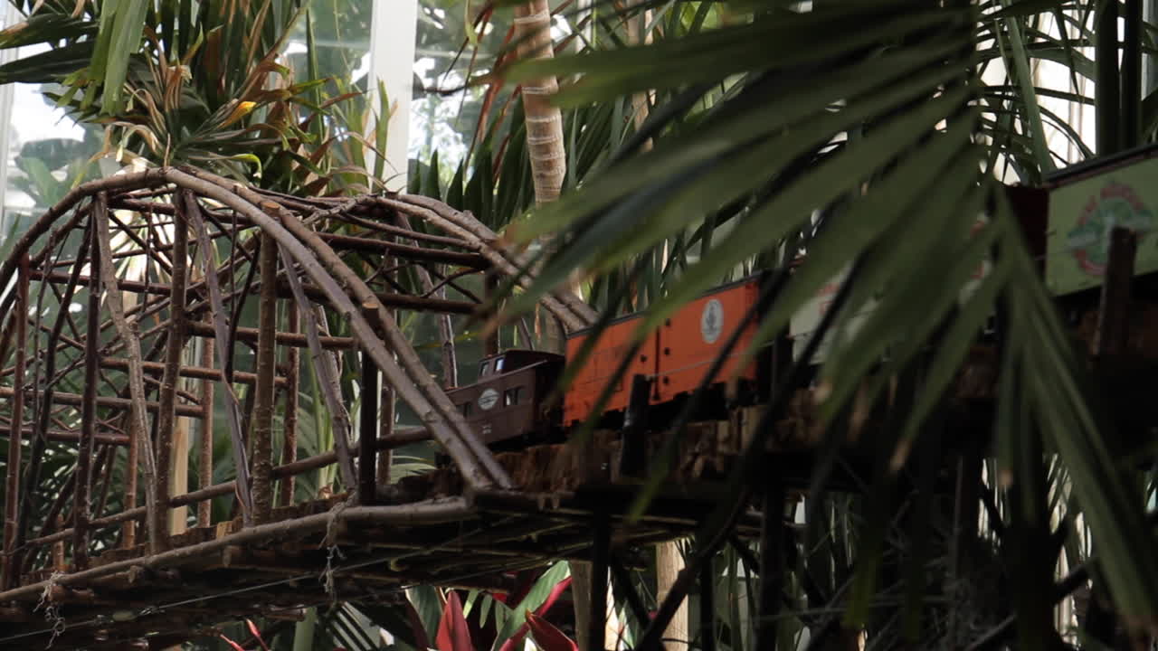 tren en miniatura pasa por un puente de madera y flores en el ferrocarril
