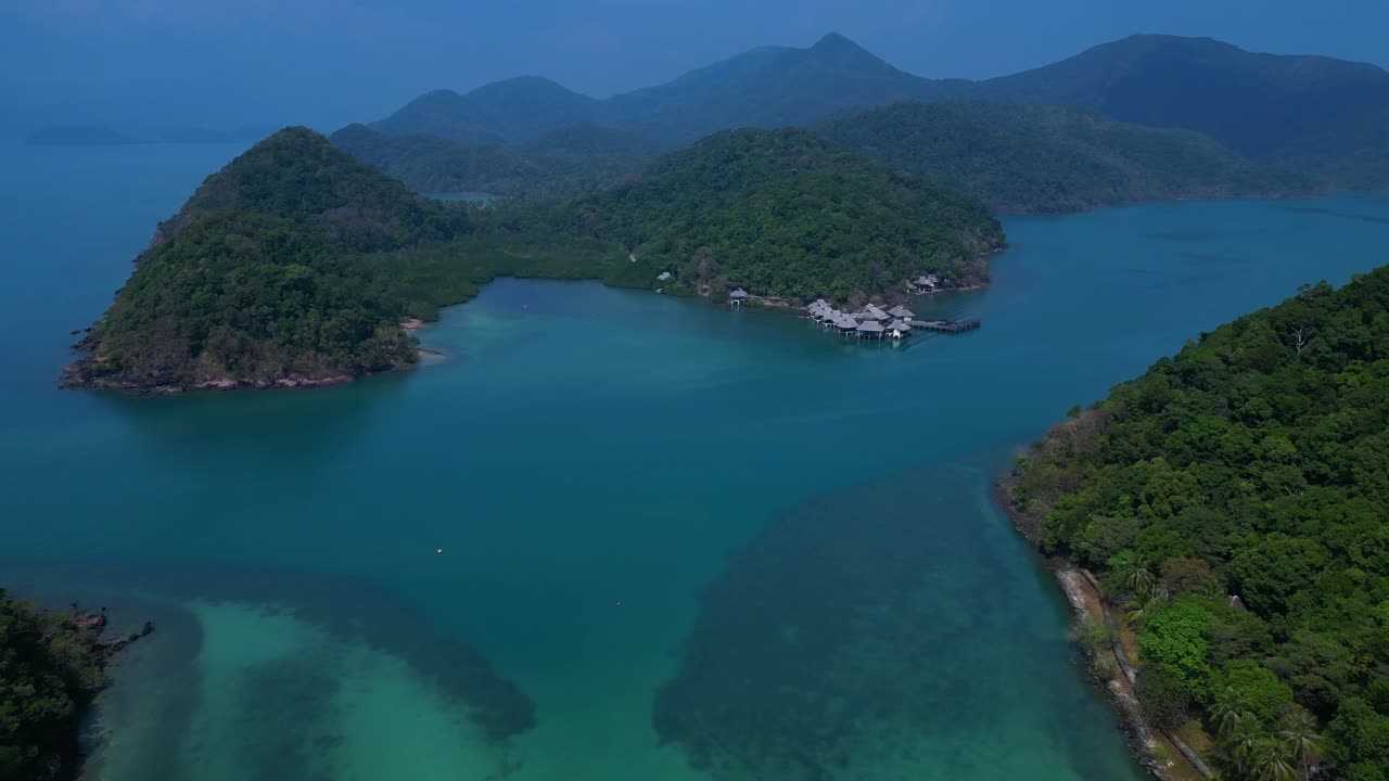 Koh Chang's Ko Ngam idyllic landscape, featuring lush greenery, a pristine beach, and a tranquil pier extending into the turquoise waters. Stunning aerial view flight fly reverse drone