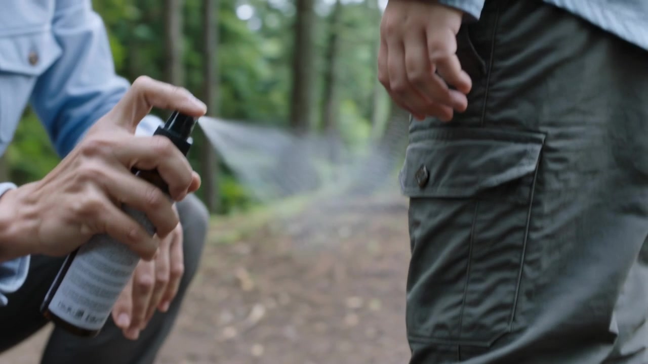 Kneeling adult rolling kid cargo pants on woods trail taking sprayer misting legs repelling ticks