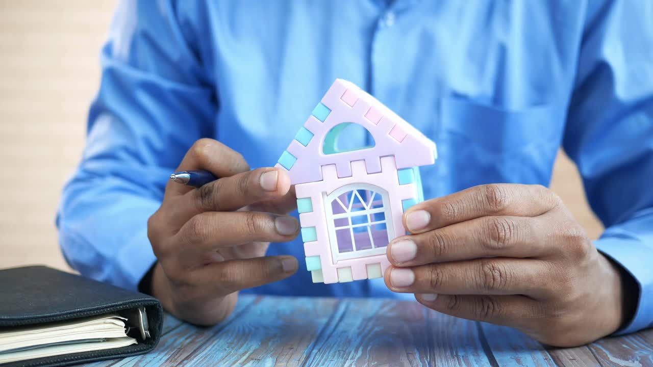hombre sosteniendo un modelo de casa en miniatura