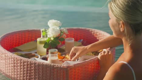 Mujer-Comiendo-Comida-Tropical-De-Un-Desayuno-Con-Bandeja-De-Corazón-Flotante-En-La-Piscina.