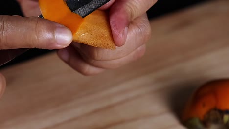 hands slicing persimmon on wooden cutting board