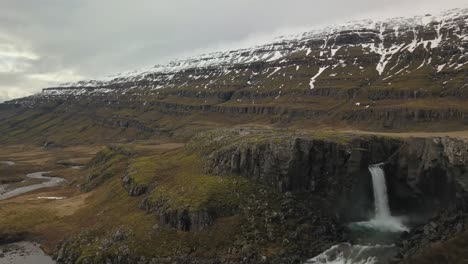 cascada que fluye hacia un exuberante valle cubierto de nieve en islandia