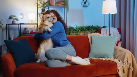 feliz mujer sonriente con cabello rizado jugando abrazo abrazo con lindo adorable perro corgi en el sofá de casa