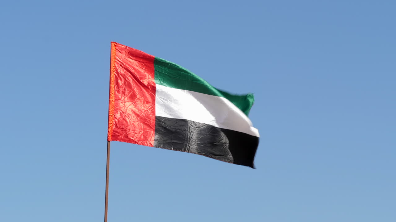 bandera de los emiratos árabes unidos ondeando en el viento frente al cielo azul
