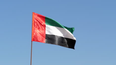 united arab emirates flag waving in the wind in front of the blue sky