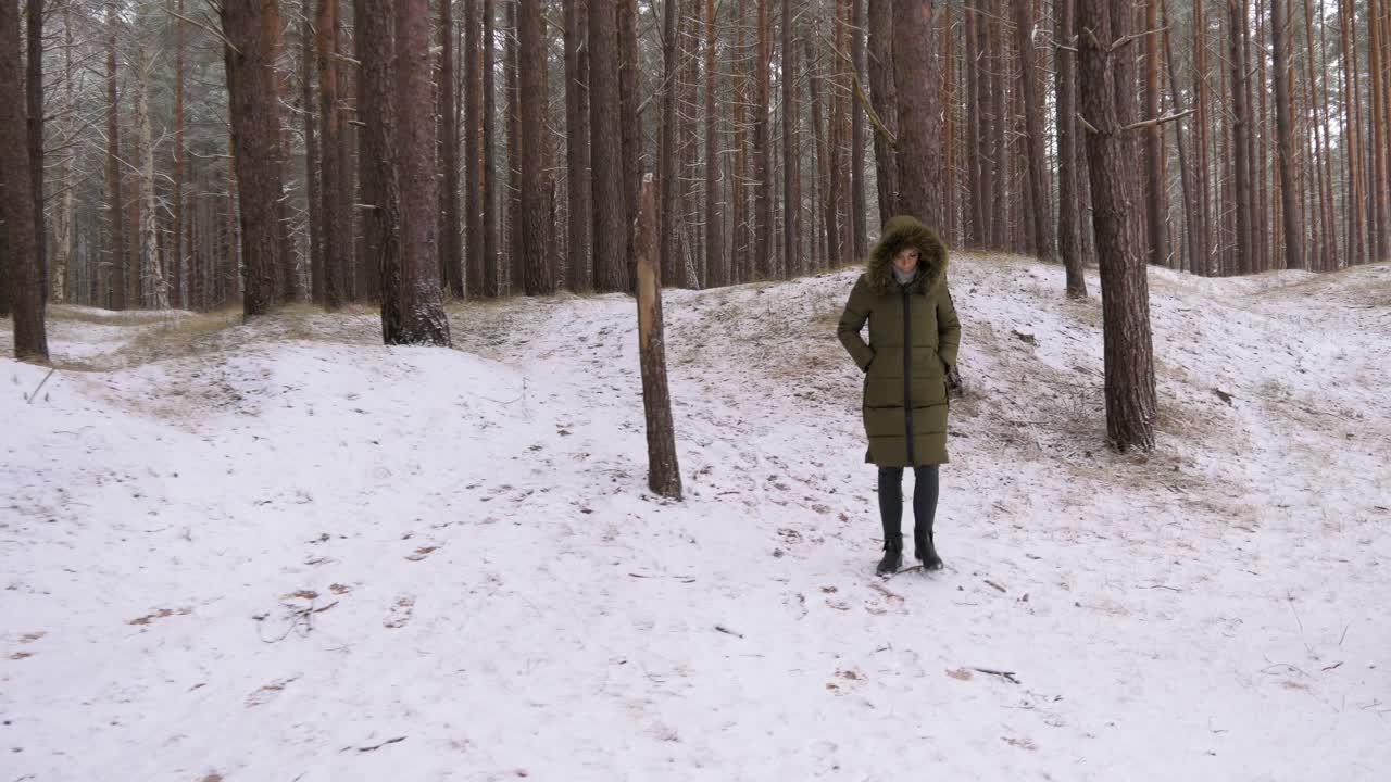 mujer joven en ropa de invierno verde camina en el bosque de pinos nevados a lo largo de la orilla arenosa de la playa del mar báltico, amplia toma de seguimiento a la derecha