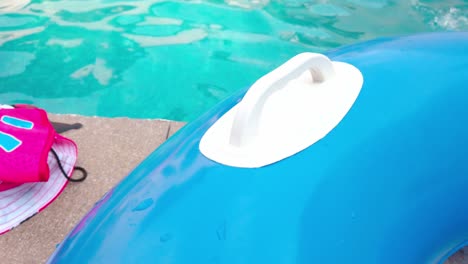 blue inflatable boat next to a swimming pool during the day, outdoor, pan shot