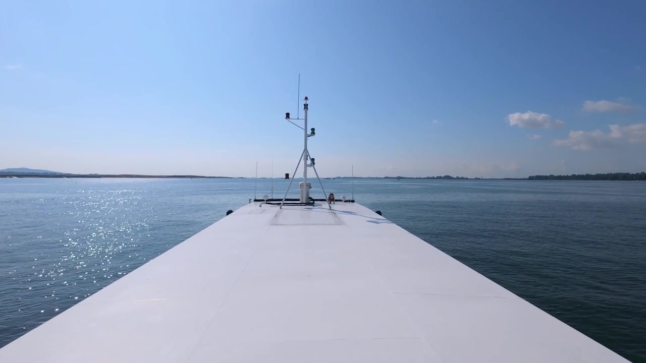 POV-Aufnahme von einem sich bewegenden Schiffsdeck, die einen langen weißen Bug und einen fernen urbanen Horizont entlang einer wichtigen Schifffahrtsroute in der Straße von Singapur zeigt