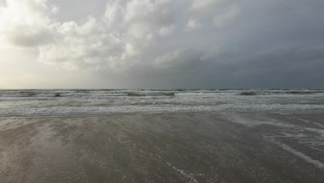 a medium-altitude drone moves backwards, facing straight towards the ocean at hvide sande, capturing the expansive sea and dramatic coastal scenery on a stormy day with a bit of beach in the frame