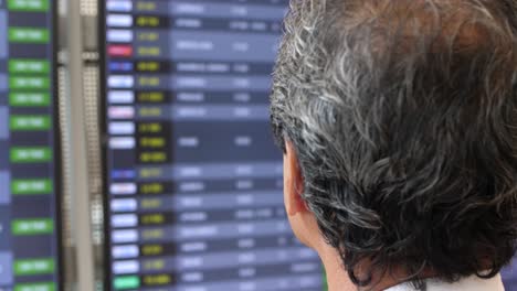 A-Japanese-businessman-stands-at-Ben-Gurion-Airport-in-Israel,-looking-at-the-arrivals-and-departures-board