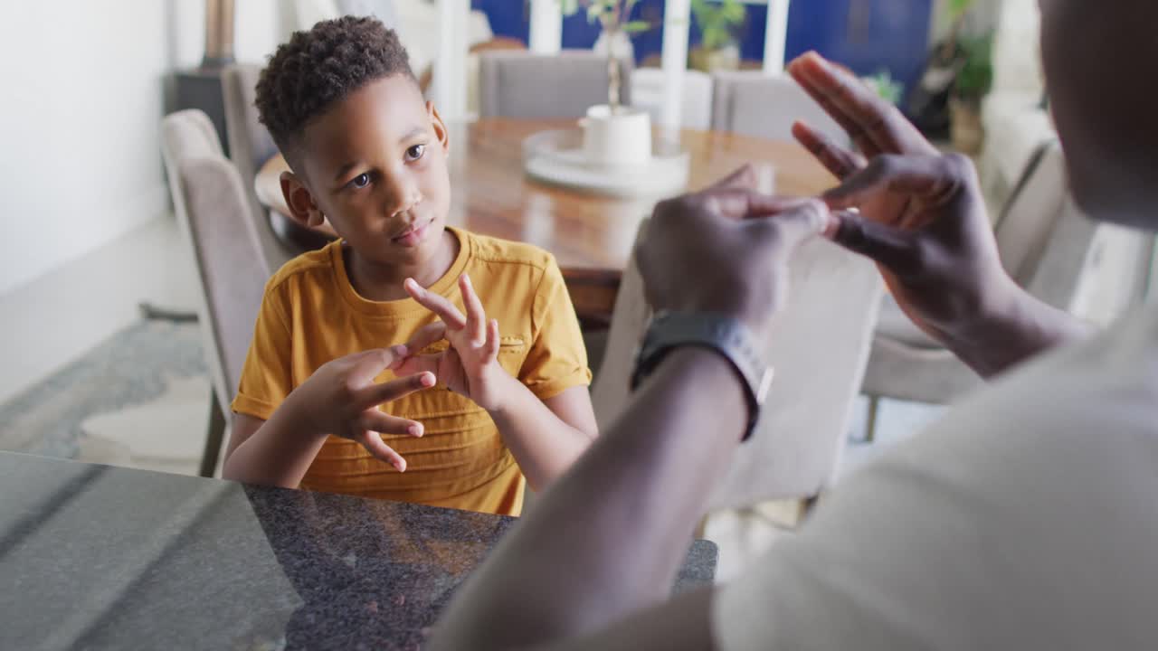 Video of happy african american father and son having fun at home, playing finger games