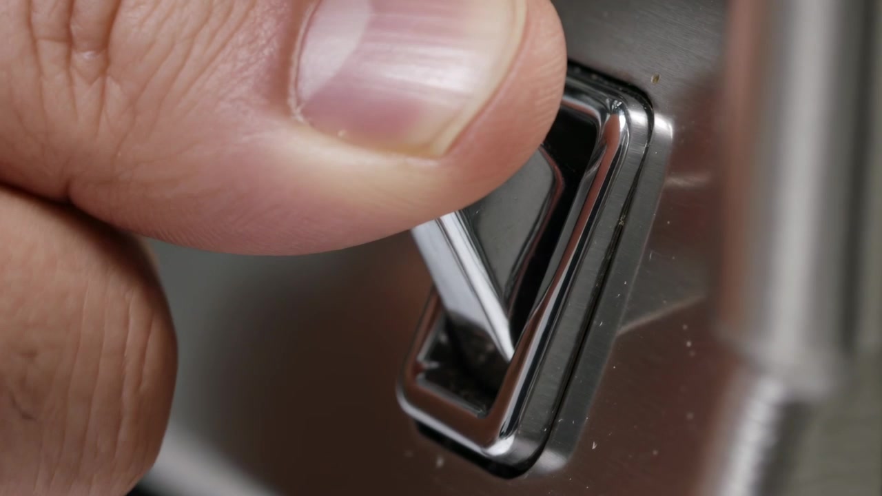 Pressing adult thumb pivoting chrome toggle on vehicle door panel, raising switch for activation