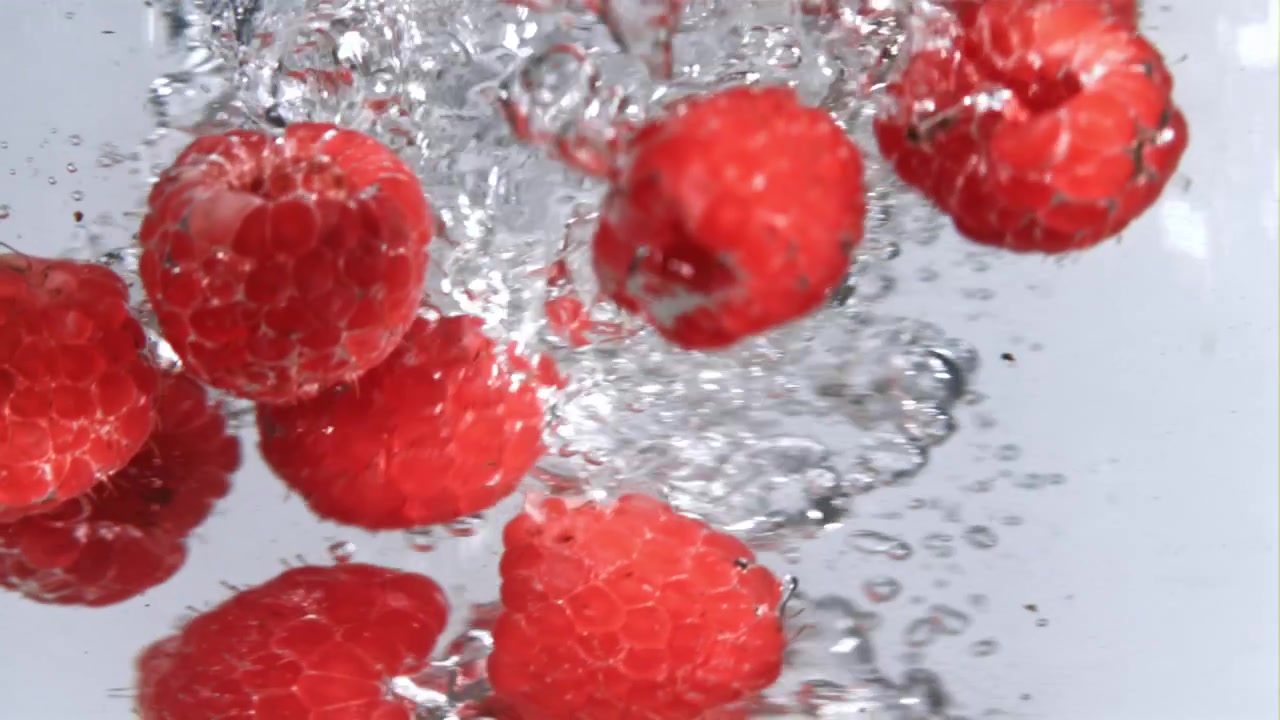 Fresh Red Raspberries Falling into Clear Water