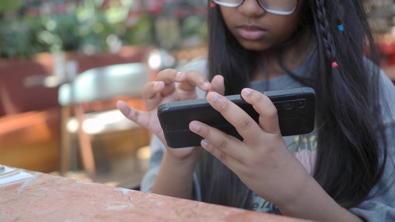 Young Girl Using Smartphone at Outdoor Cafe Table