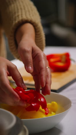 video vertical de cerca de una mujer en casa en la cocina preparando verduras frescas saludables para una comida vegetariana o vegana cortando pimientos rojos en la tabla 1