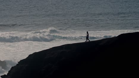 a young couple walks hand in hand along a rugged volcanic cliff overlooking the atlantic ocean in lanzarote, canary islands, spain.
