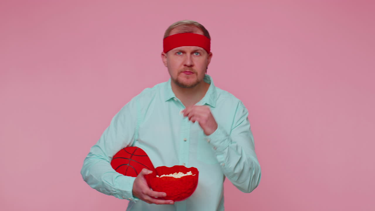 Vousatý mladý muž, fanoušek basketbalu, jedící popcorn, dělající vítězné gesto, oslavující vítězství