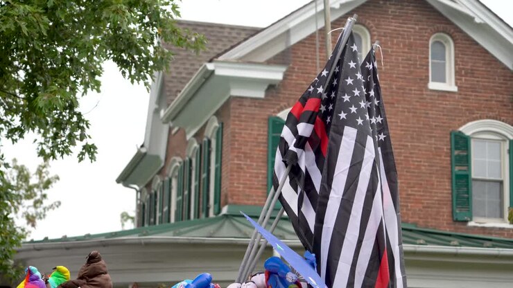 American flags set against an old building in a small town at a festival with some of the flags having the thin red line which honors fire fighters