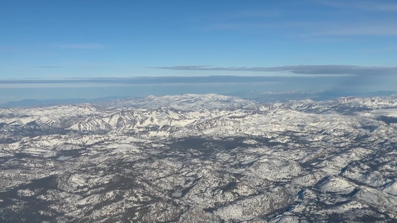 巡航高度から撮影された壮大な空撮は、鮮やかな青空の下、地平線まで続く広大な雪に覆われた山脈を映し出している。険しい山頂と尾根には雪が薄く積もっており...
