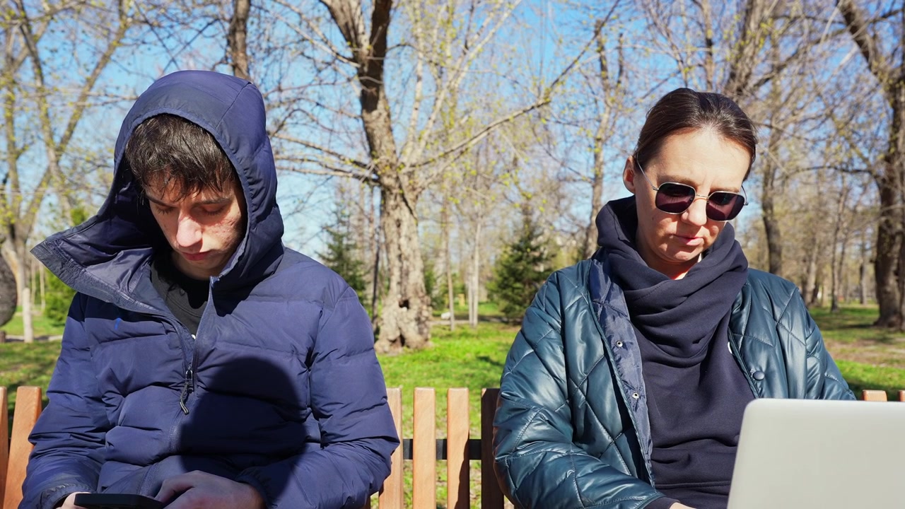 Young Couple Using Digital Devices on a Park Bench
