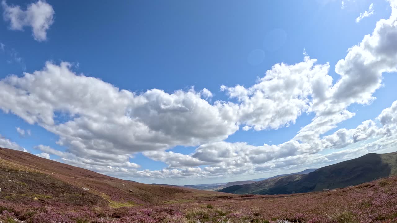 Dynamic time-lapse of cumulus clouds drifting above heather-covered hills and Loch Brandy, with bright daylight and wide landscape perspective