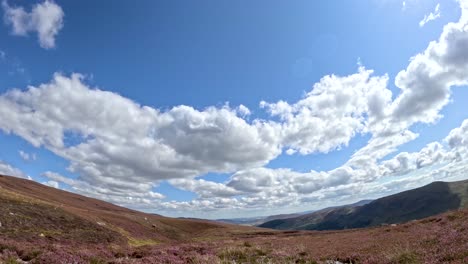 dynamic time-lapse of cumulus clouds drifting above heather-covered hills and loch brandy, with bright daylight and wide landscape perspective