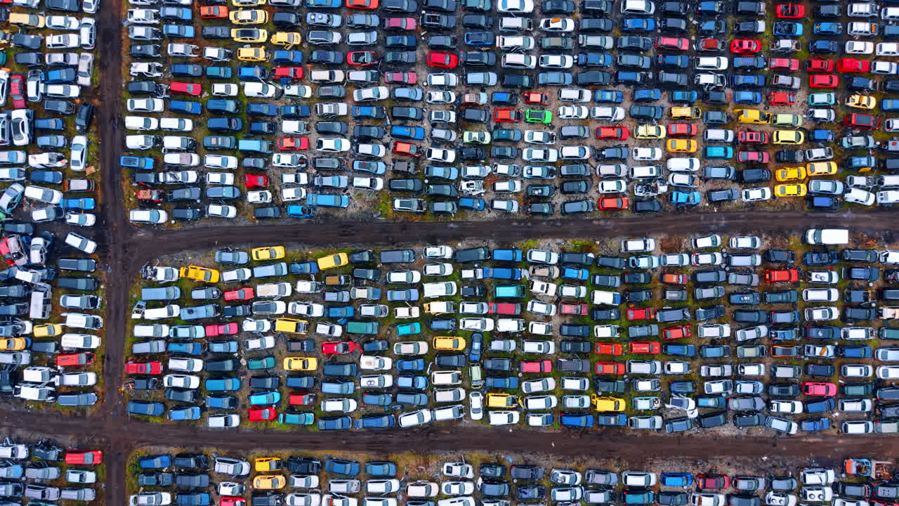Bredt luftfoto af et massegenbrugsanlæg for køretøjer. Detaljeret top-down droneudsigt over hundredvis af skrotbiler parkeret i tætte rækker på et bilgenbrugscenter.