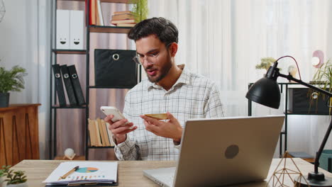 happy indian businessman using bank credit card and smartphone for online shopping bill payments