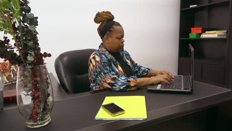 african american business owner typing on computer and checking phone for messages productive multi tasking telecommuting