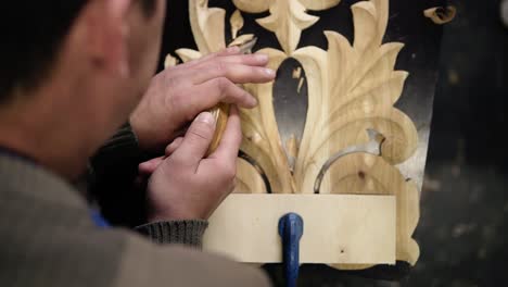 Close-up-footage-of-man's-hands,-he-is-curving-a-small-details-on-the-piece-wodden-pattern---floral-ornament-in-work-shop-on-the-work-table-using-small-planer.-Footage-from-the-top