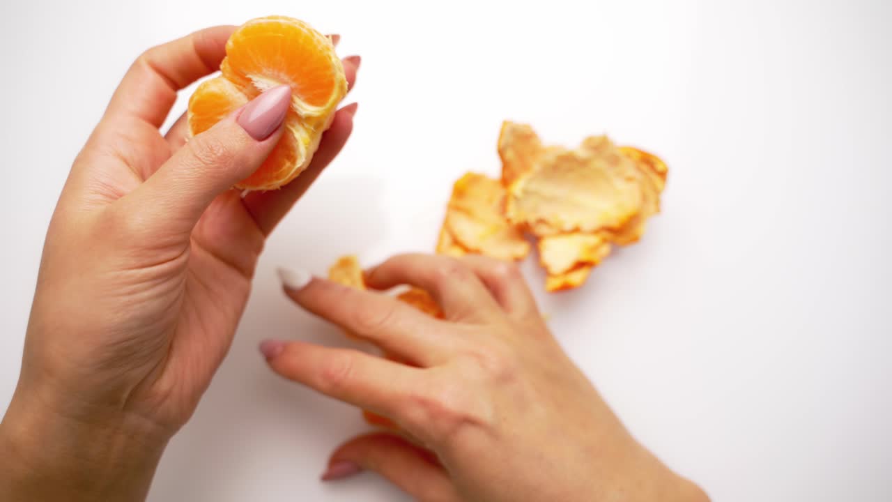 Hands clean tangerine with slices. Peeling process of mandarin on white background