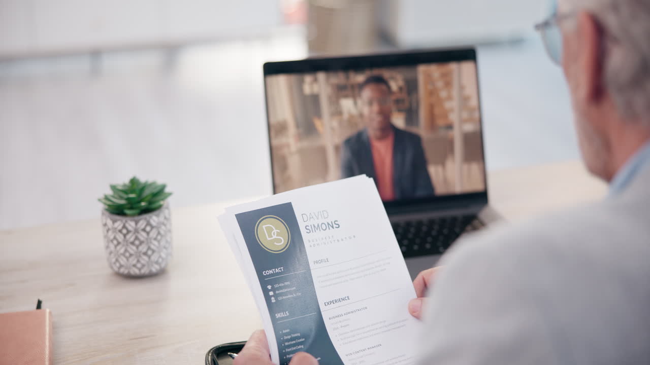 Senior Man Conducting a Video Call Job Interview While Holding a Resume