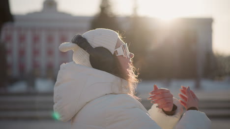 close up of student wearing winter coat, dancing with visible breath in cold air while sunlight flares in background, headphones on, relaxed expression, joyful winter vibe captured in sunset