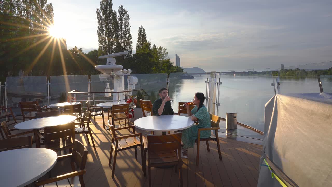 Young couple in love having a drink at a pier table in a pleasant sunset