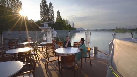 young couple in love having a drink at a pier table in a pleasant sunset