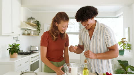 diverse couple laughing while cracking eggs into bowl in bright kitchen, at home