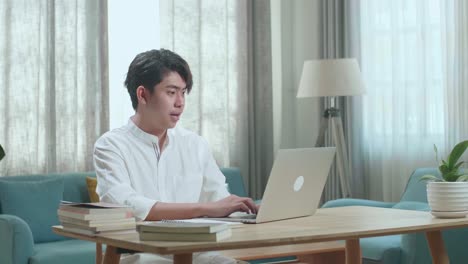asian man student celebrating while using computer to study online at home