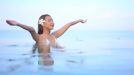 Close-up-of-an-attractive-woman-with-a-flower-behind-her-right-ear-standing-in-a-resort-pool-enjoying-the-warm-water