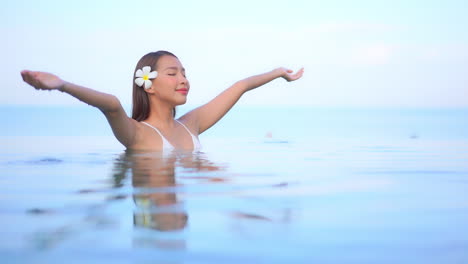 close up of an attractive woman with a flower behind her right ear standing in a resort pool enjoying the warm water