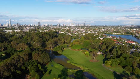 drone footage captures the gold coast skyline with lush greenery in the foreground under clear blue skies