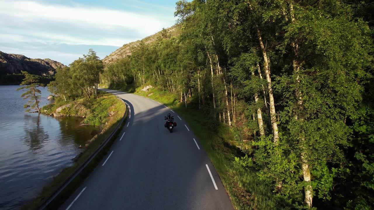 En motorcyklist kører langs en sø i bjergene