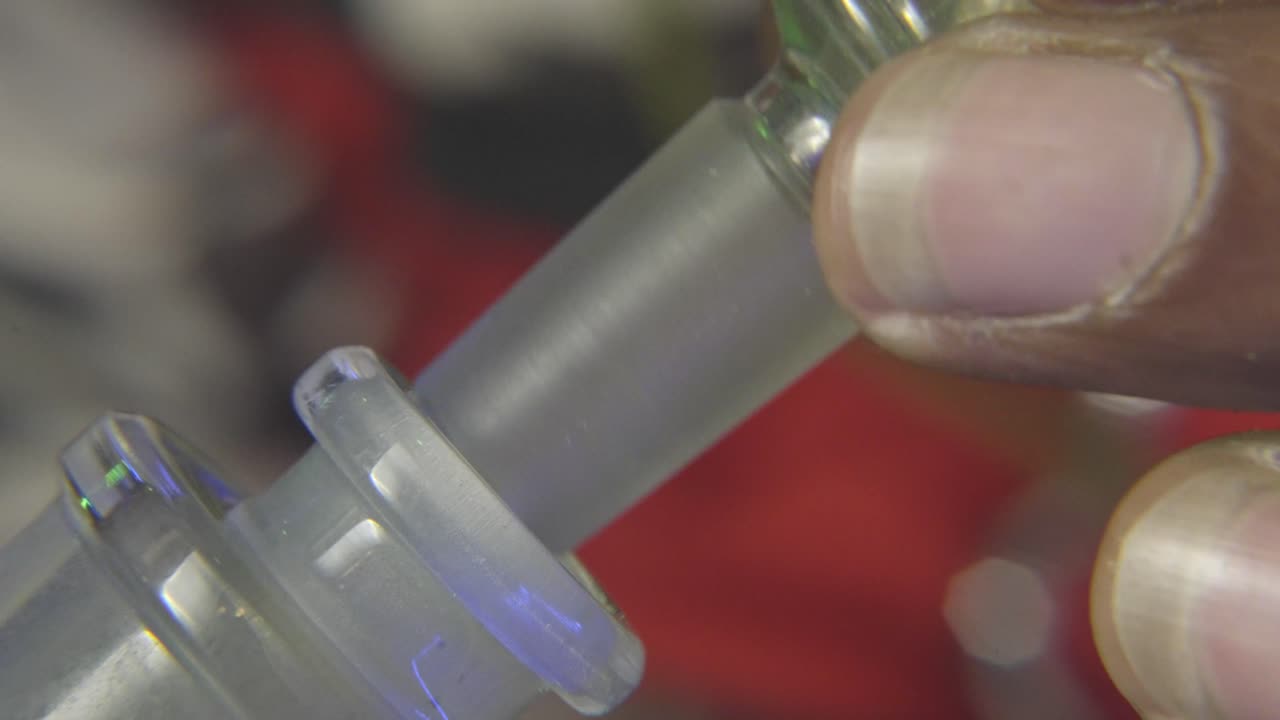 vista lateral de la mano de un hombre negro colocando el tallo de un cuenco de vidrio lleno de marihuana en un bong de agua que se utiliza para fumar marihuana