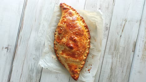 calzone dorado horneado en una mesa de madera blanca rústica
