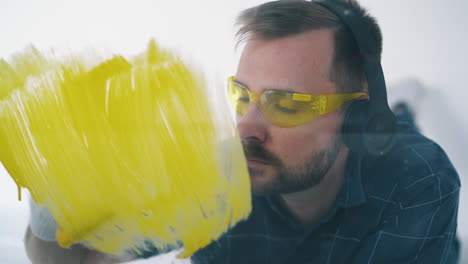 man with headphones paints wall with yellow color in room