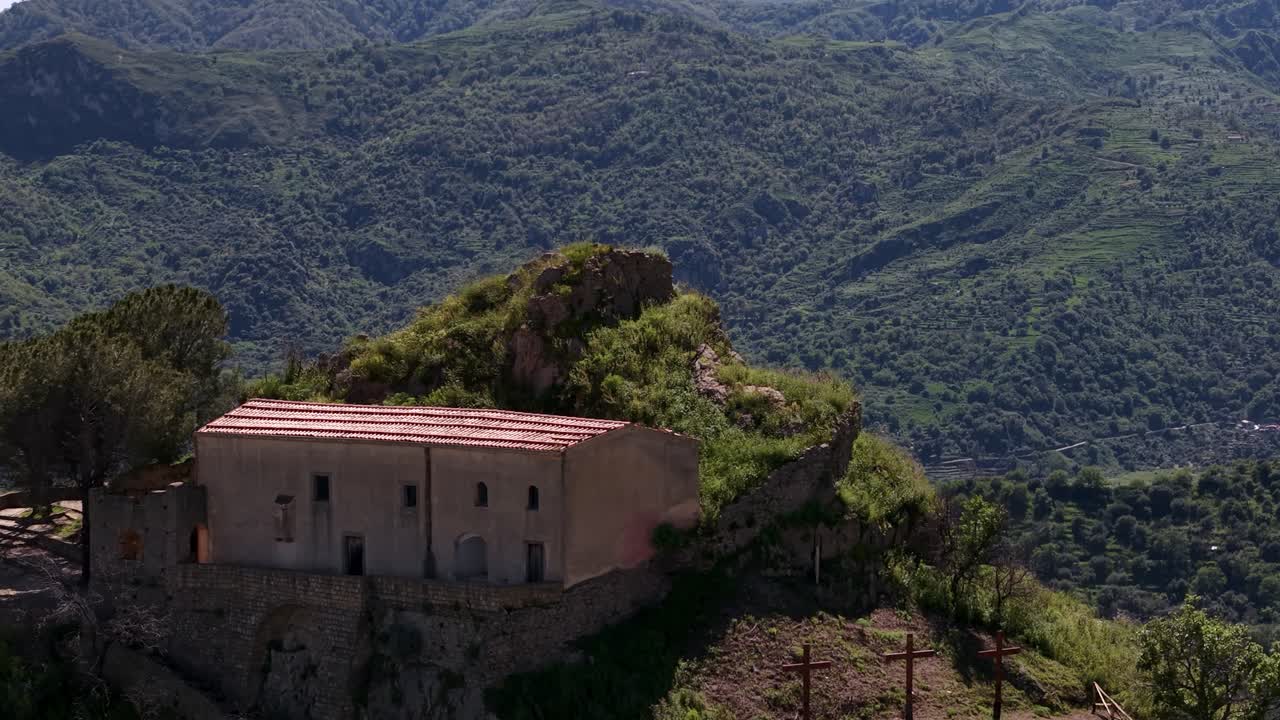Ripresa aerea con tilt up che rivela il Castello di Pentefur tra le montagne verdi di Savoca, Sicilia, Italia.