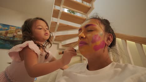 little girl applying makeup to her pregnant mother at home